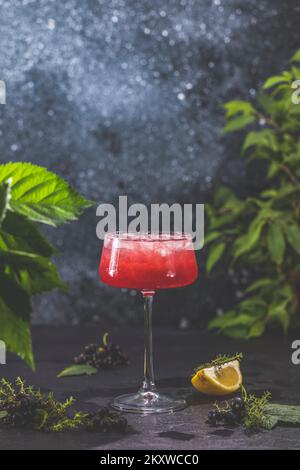 Élégant verre de Black Currant Gin Sour cocktail ou Mockttails entouré d'ingrédients sur une surface de table sombre. Boisson rafraîchissante prête à boire. Banque D'Images