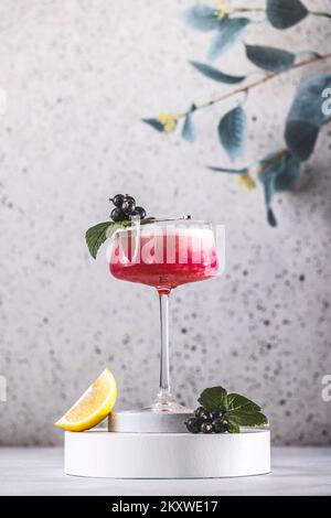 Élégant verre de Black Currant Gin Sour cocktail ou de queues de macktoes entouré d'ingrédients sur la surface de table grise. Boisson rafraîchissante prête à boire. Banque D'Images