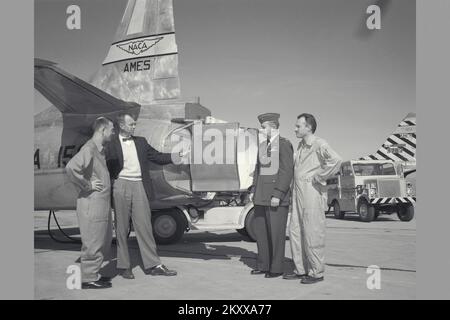 George Cooper, pilote d'essai en chef d'Ames, discute des phases des essais d'évaluation en vol. Personnel du NACA (de l à R) le major de la Force aérienne E. Sommerich; l'ingénieur Ames Seth Anderson, le lieutenant-colonel Tavasti; et George Cooper posent devant l'inverseur de poussée sur le F-94C01. Banque D'Images