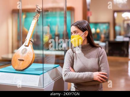 Femme en masque regardant des collections d'instruments de musique anciens dans le musée Banque D'Images