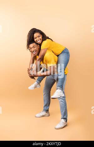 Jeune homme noir qui donne le pigegyback à sa petite amie sur fond de studio pêche, pleine longueur de prise de vue Banque D'Images