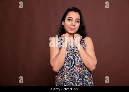 Femme indienne souriante tenant des poings serrés sur le portrait des joues, posture mignonne. Dame gaie touchant le visage avec les mains, jeune personne debout avec insouciance expression, regardant la caméra Banque D'Images