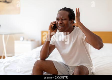 Appel désagréable. Portrait de l'homme noir stressé parlant au téléphone portable dans la chambre Banque D'Images