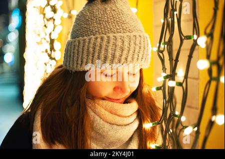 Souriant une jolie jeune femme avec un chapeau d'hiver sur le fond illuminé des lumières de Noël du nouvel an Banque D'Images