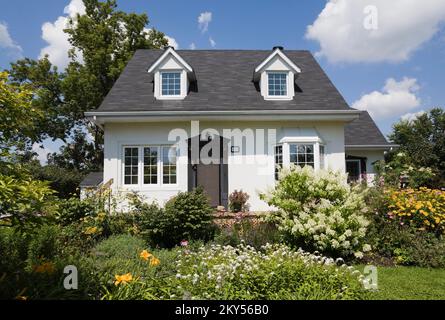 Maison de style manoir Canadiana à deux étages blanc avec bordure noire avec jardin paysagé en été. Banque D'Images