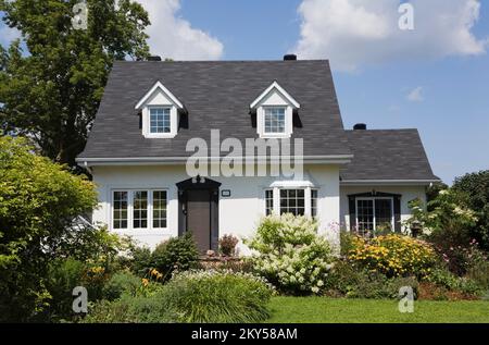 Maison de style manoir Canadiana à deux étages blanc avec bordure noire avec jardin paysagé en été. Banque D'Images