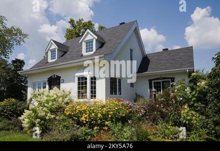 Maison de style manoir Canadiana à deux étages blanc avec bordure noire avec jardin paysagé en été. Banque D'Images