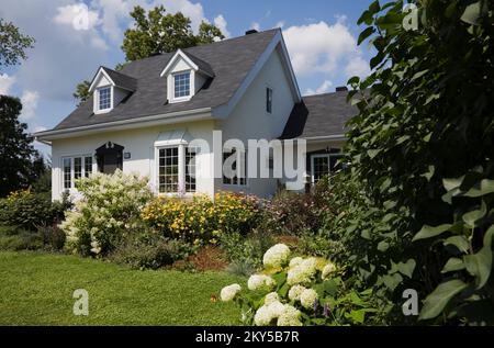 Maison de style manoir Canadiana à deux étages blanc avec bordure noire avec jardin paysagé en été. Banque D'Images