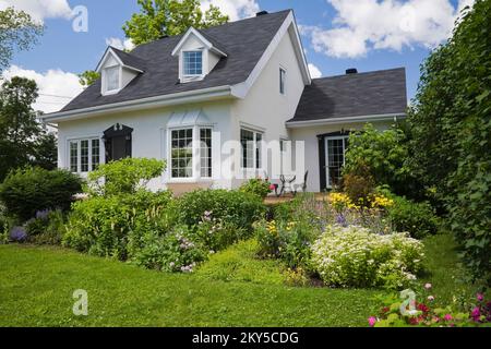 Maison de style manoir Canadiana à deux étages blanc avec bordure noire avec jardin paysagé en été. Banque D'Images