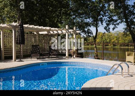 Piscine creusée avec mobilier de jardin paysager en été. Banque D'Images