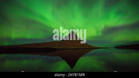 Des aurores vibrantes tourbillonnent au-dessus de Kirkjufell, en Islande, illuminant le ciel et se reflétant sur le paysage serein en contrebas dans un spectacle éblouissant de la nature Banque D'Images