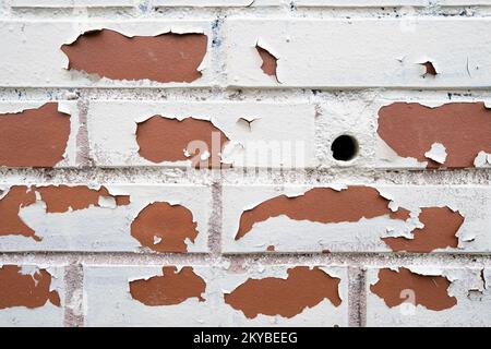 Nouveau mur en brique rouge avec un petit trou rond et peinture blanche qui s'écaille. Arrière-plan abstrait. Copier l'espace. Banque D'Images