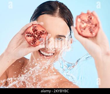 Portrait, soin de la peau et grenade par femme dans l'eau pour le bien-être, le nettoyage et la santé de la peau sur fond bleu. Beauté, éclaboussures et fruits Banque D'Images