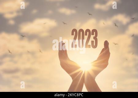 Mains tenant la silhouette du nouvel an 2023 sur fond de coucher de soleil Banque D'Images