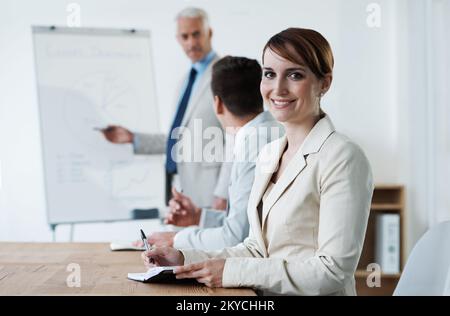 Shes a pris l'avantage de l'entreprise. Les hommes d'affaires se sont rassemblés autour d'une table pendant que leur responsable donne une présentation. Banque D'Images