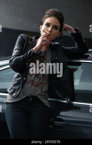 Attitude et attractive. Une jeune femme rebelle qui a l'air de fumer une cigarette dans un garage de voiture. Banque D'Images