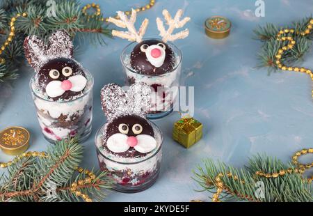 Gâteau dans des verres en forme de lapins et de cerfs mignons avec cerises, biscuit au chocolat et flocons de noix de coco sur fond bleu Banque D'Images