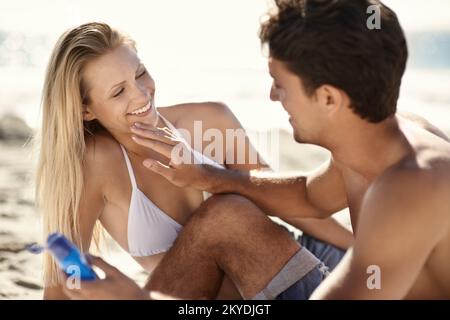 Amusez-vous avec la crème solaire. Un jeune couple appliquant de la crème solaire à la plage. Banque D'Images