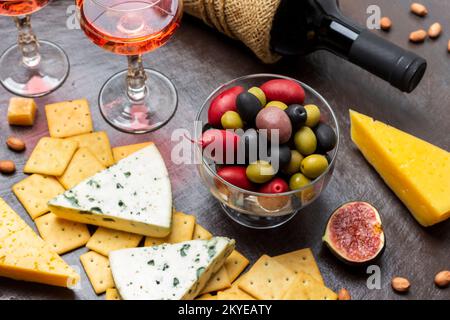 Olives multicolores dans un bol en verre. Fromage et biscuits et un demi-figue. Bouteille de vin et deux verres de vin rouge. Vue de dessus. Arrière-plan marron. Banque D'Images