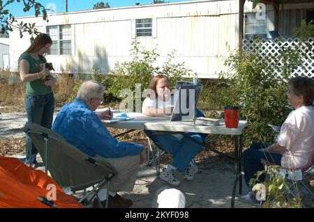 Ouragan Katrina, Wiggins, Mils., 29 octobre 2005 -- en face de sa maison mobile, Cheryl Rasbury (au centre) regarde des photos de sa maison de plage démolie par l'ouragan Katrina. Sa fille Emily a un chiot (nommé « FEMA ») tandis que l'employée de la FEMA, Alan Jones prend des notes et que l'amie de la famille Gilda Tackett regarde. George Armstrong/FEMA Banque D'Images