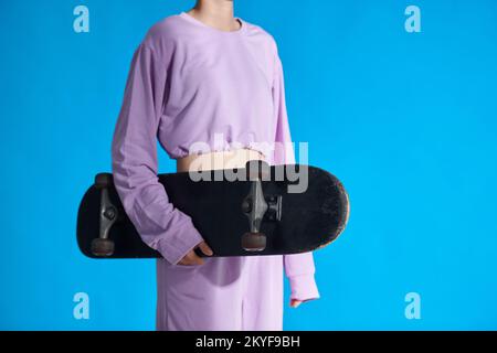 Image rognée d'une fille en haut lavande et en haut de la tenue de planche à roulettes Banque D'Images