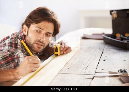 Obtenir les mesures appropriées. Un beau jeune menuisier mesurant et marquant le bois. Banque D'Images