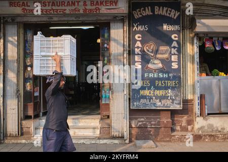 Un homme portant une boîte de marchandises sur sa tête, passant par Regal Restaurant & Bakery, un ancien restaurant iranien de Byculla, Mumbai, Inde Banque D'Images