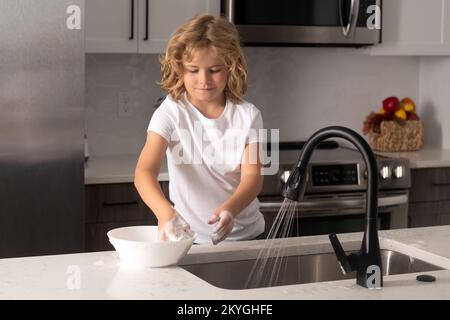 Vaisselle de nettoyage pour enfants avec éponge. Fournitures de nettoyage. Aide au nettoyage. Tâches d'entretien ménager. Vaisselle de lavage pour enfants. Enfant garçon lave les plats dans la cuisine Banque D'Images