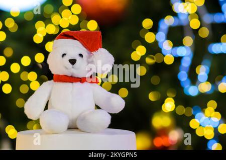 Accent sélectif sur les yeux des ours en peluche du Père noël qui portent un chapeau assis devant les lumières bokeh colorées de l'arbre de Noël. Banque D'Images
