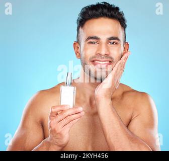 Portrait de l'homme, parfum et après-rasage produit de bouteille pour les soins de la peau, le bien-être et les cosmétiques de luxe sur fond bleu. Joyeux jeune indien, homme Banque D'Images