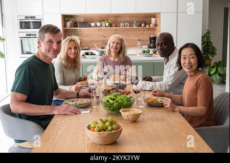 Groupe de divers amis seniors réunis pour déjeuner dans la cuisine Banque D'Images