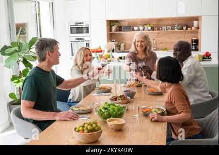 Photo de mi-plan de divers collègues qui portent un toast alors qu'ils sont réunis à la maison pour le déjeuner Banque D'Images