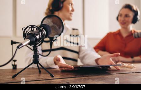 Deux femmes ayant une conversation tout en enregistrant un podcast Internet dans un studio à domicile. Deux créateurs de contenus féminins co-hébergent une diffusion audio pour TH Banque D'Images