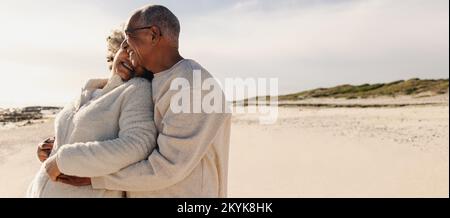 Tomber amoureux de la plage. Couple de personnes âgées heureux souriant et s'embrassant tout en se tenant sur le sable de la plage. Couple senior joyeux appréciant le thei Banque D'Images