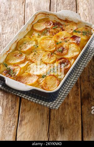 Tranches de cocotte de pommes de terre avec oignons, thym frais et beurre dans le plat de cuisson sur la table. Verticale Banque D'Images