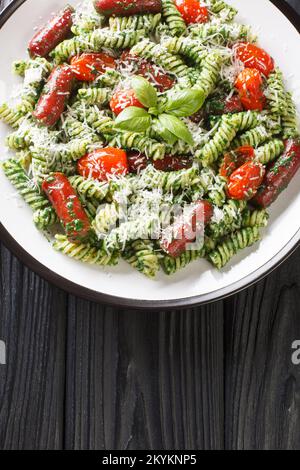 Plat de pâtes copieux avec pesto génois, saucisse, tomates et parmesan sur l'assiette de la table. Vue verticale du dessus Banque D'Images