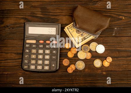 Billets en dollars, pièces en euros, portefeuille en cuir brun vintage et calculatrice sur une surface en bois. Gros plan, mise au point sélective. Banque D'Images