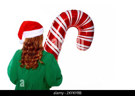 Fille de Noël tenant un énorme ballon de canne dans les mains, portant dans la robe verte, chapeau de père noël et chaussettes chaudes rouges pour la fête de la nouvelle année Banque D'Images