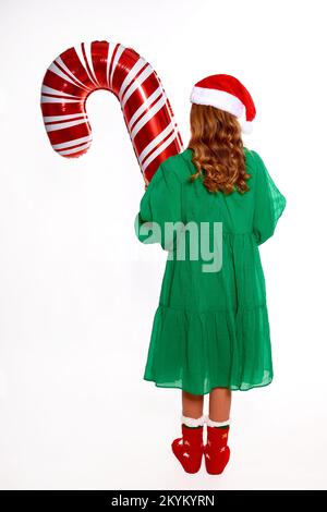 Fille de Noël tenant un énorme ballon de canne dans les mains, portant dans la robe verte, chapeau de père noël et chaussettes chaudes rouges pour la fête de la nouvelle année Banque D'Images