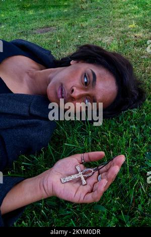 gros plan d'une jeune femme qui pose sur l'herbe avec un ankh d'or dans sa main Banque D'Images
