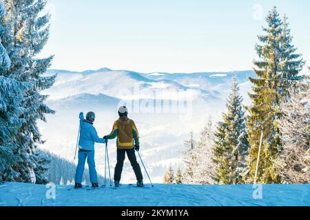 Couple heureux sur la station de ski. Homme et femme sur les skis tenant les mains et regardant les montagnes. Des vacances d'hiver incroyables Banque D'Images