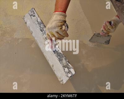 mains d'un plâtrier avec deux spatules au travail près du mur, travaux de construction sur le plâtrage, nivellement et remplissage des murs avec un outil à main Banque D'Images