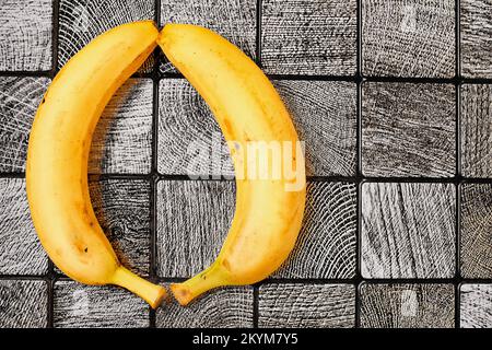 Deux bananes jaunes mûres sur une surface grise carrelée de carreaux. Espace pour le texte Banque D'Images