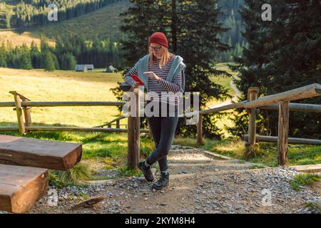 Explorer woman using mobile phone pour la navigation. Femme transportant des sacs de voyage marche à travers une forêt. Banque D'Images