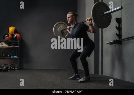 Homme levant la barbell dans le cadre de l'entraînement crossfit dans la salle d'entraînement sombre. Espace pour le texte Banque D'Images