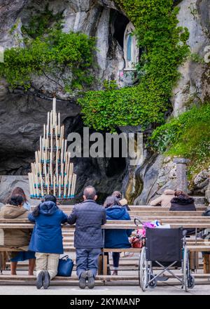 Pèlerins priant devant la Grotte de Lourdes avec la statue de Bernadette Soubirous en arrière-plan (France) Banque D'Images