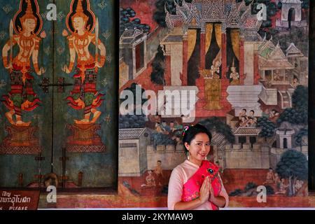 Une dame thaïlandaise en costume de mon sourit et met les mains ensemble en hommage au mur mural du temple Banque D'Images