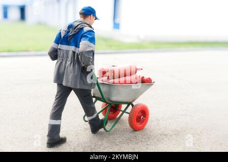 Les vêtements d'homme au travail portent des extincteurs rouges dans la brouette. Recyclage industriel et recharge des extincteurs. Agent d'extinction d'incendie. Banque D'Images