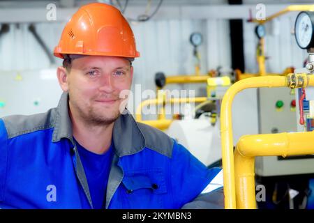 Portrait d'un ingénieur dans un casque de construction et des vêtements de travail sur fond industriel à l'intérieur des locaux. Employé de l'industrie du gaz à l'intérieur de la chaufferie. Début de la saison de chauffage en Europe. Banque D'Images