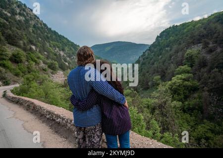 couple dans les montagnes se réjouissent dans leur voyage. Ils embrassent d'une main, se tiennent avec leur dos au public et regardent les montagnes. Banque D'Images